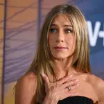 Láttál már matt arany zongorát? Jennifer Aniston gyönyörű nappalijában modern festmény és fa falszakasz mellett áll